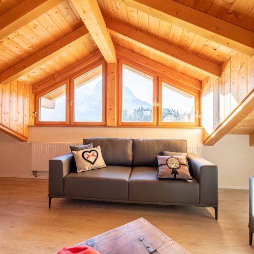 Wohnzimmer mit schwarzem Sofa und Ausblick in Ferienwohnung in Garmisch-Partenkirchen