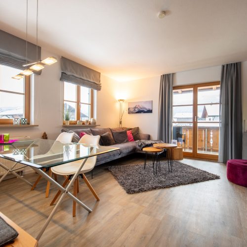 Wohnzimmer und Esszimmer mit Glastisch und grauem Sofa in Ferienwohnung in Garmisch-Partenkirchen
