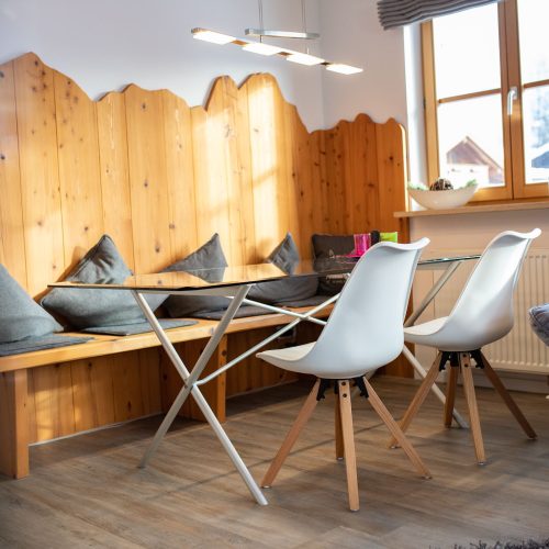Essbereich mit einer Holzbank mit Kissen und zwei weißen Stühlen in Ferienwohnung in Garmisch-Partenkirchen