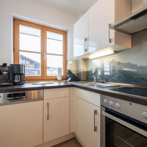 Küche in weiß mit einer dunklen Arbeitsfläche in Ferienwohnung in Garmisch-Partenkirchen