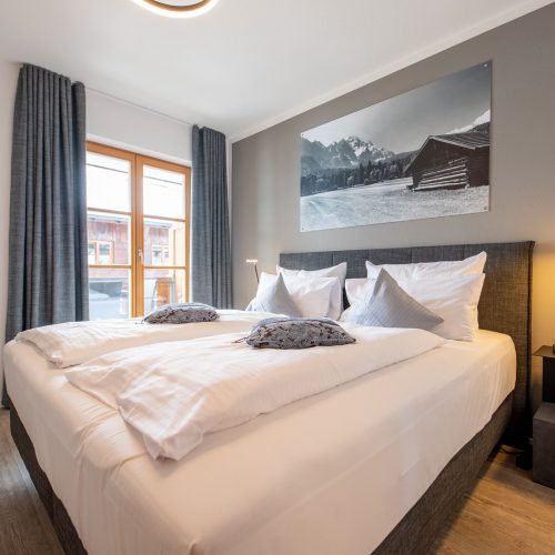 Schlafzimmer mit dunkelgrauem Bett und hellgrauer Wand in Ferienwohnung in Garmisch-Partenkirchen
