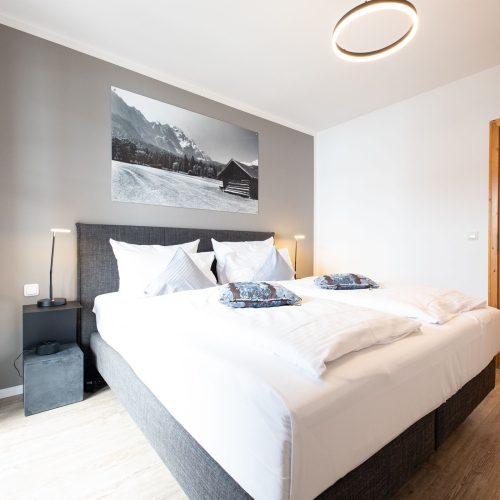 Doppelbettzimmer mit einer grauen Wand und Nachtschränken in Ferienwohnung in Garmisch-Partenkirchen