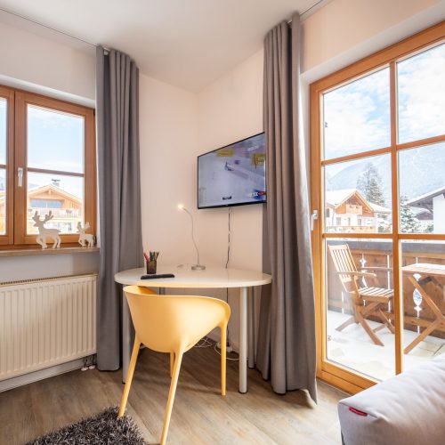 Wohnzimmer mit einem kleinen Tisch mit einem Stuhl, einem Fernseher und einem Ausgang zu dem Balkon in Ferienwohnung in Garmisch-Partenkirchen