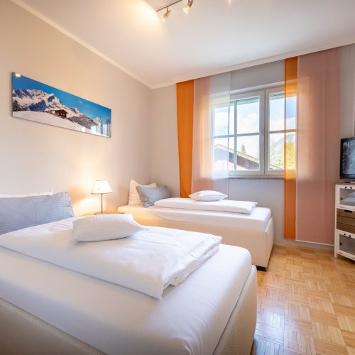 zwei Einzelbetten mit Fernseher und Schrank in Ferienwohnung in Garmisch-Partenkirchen