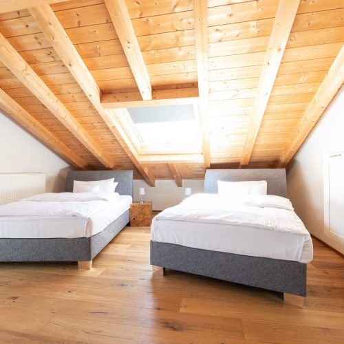 Zwei Betten im Schlafzimmer mit Regal und Blumen in Ferienwohnung in Garmisch-Partenkirchen