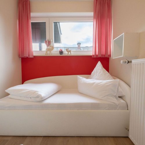 Einzelbett mit roter Wand in Ferienwohnung in Garmisch-Partenkirchen