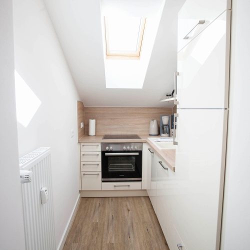 Küche in weiß mit hell braunen Arbeitsflächen und einer Schräge mit Dachfenster in Ferienwohnung in Garmisch-Partenkirchen