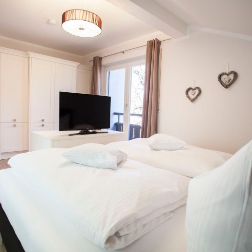 Doppelbett mit einem Fernseher und einem großen weißen Kleiderschrank in Ferienwohnung in Garmisch-Partenkirchen