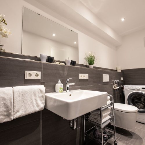 Badezimmer mit dunklen Fliesen und einem weißen Waschbecken in Ferienwohnung in Garmisch-Partenkirchen