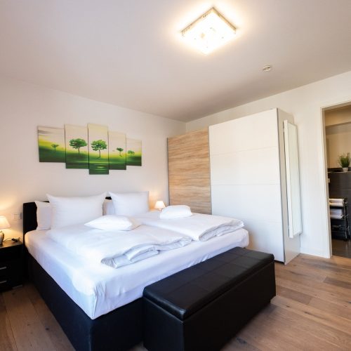 Doppelbett in schwarz mit schwarzen Nachttischen und einem Bild von Bäumen in Ferienwohnung in Garmisch-Partenkirchen