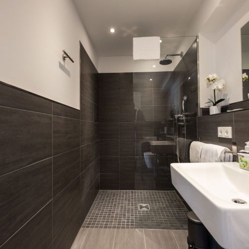 Badezimmer mit dunklen Fliesen und einer großen Dusche in Ferienwohnung in Garmisch-Partenkirchen