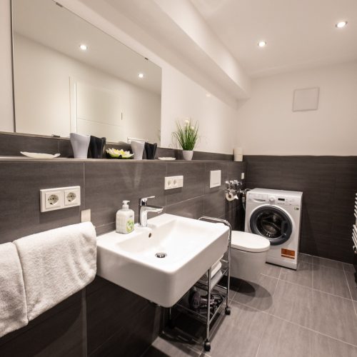 Badezimmer mit dunklen Fliesen und einer Waschmaschine in Ferienwohnung in Garmisch-Partenkirchen