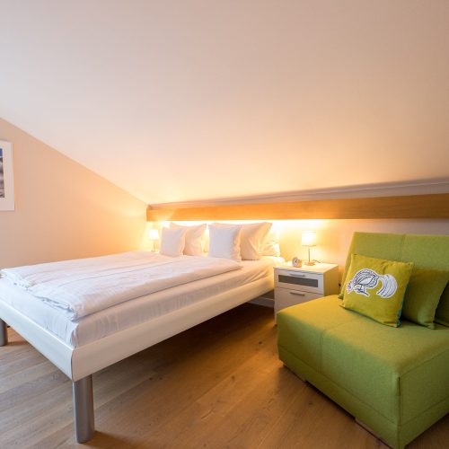 Schlafzimmer mit grünem Sessel und weißem Bett in Ferienwohnung in Garmisch-Partenkirchen