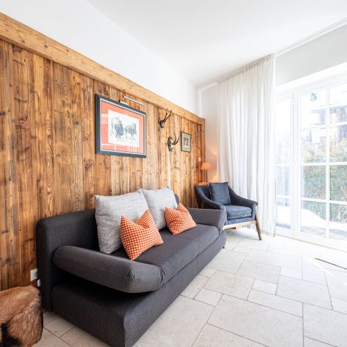 Sofa in anthrazit mit Kissen und einem gepolsterten grauen Stuhl an der Holzwand in Ferienwohnung in Garmisch-Partenkirchen