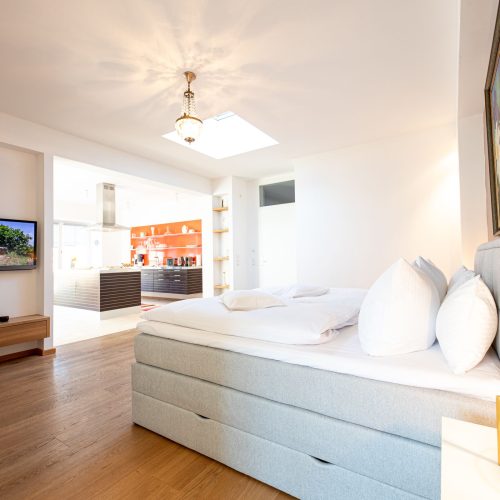 offenes Schlafzimmer mit Fernseher und Sideboard und blick in die Küche in Ferienwohnung in Garmisch-Partenkirchen