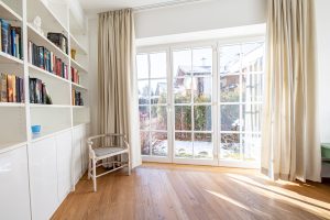 Fensterfront mit creme farbenen Vorhängen und einem kleinen Stuhl in Ferienwohnung in Garmisch-Partenkirchen