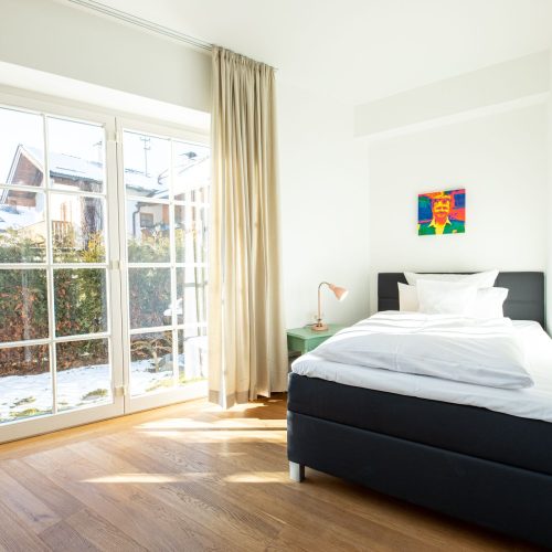 mittelgroßes Bett in schwarz mit pastell-grünem Beistelltisch und einer rosanen Lampe in Ferienwohnung in Garmisch-Partenkirchen