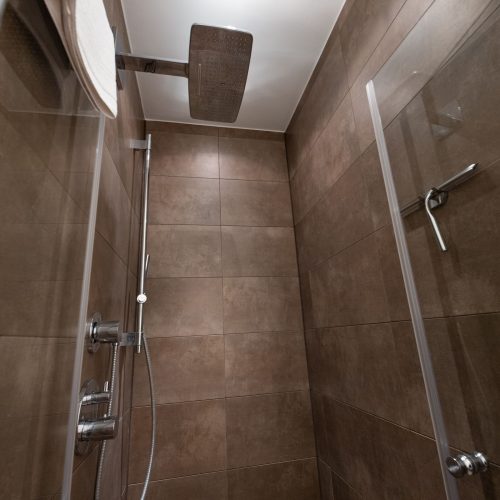 dunkel gehaltene Dusche mit dunkel braunen Fliesen und einer Regendusche in Ferienwohnung in Garmisch-Partenkirchen