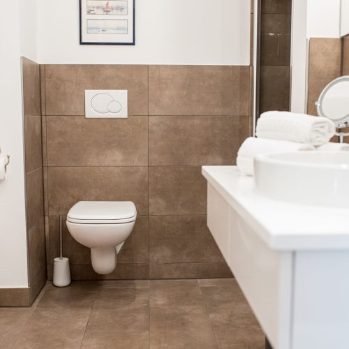 Dunkle Fliesen in einem braun Ton mit weißer Toilette und weißen Waschbecken in Ferienwohnung in Garmisch-Partenkirchen