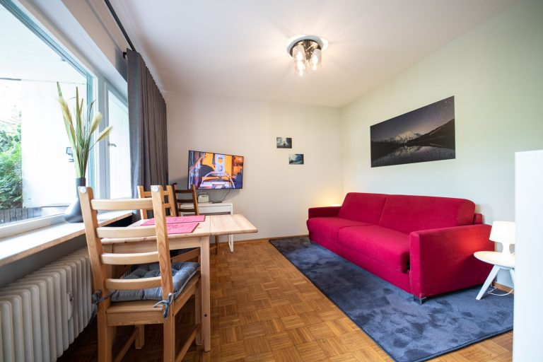 rotes Sofa mit einem dunklen Teppich in Ferienwohnung in Garmisch-Partenkirchen