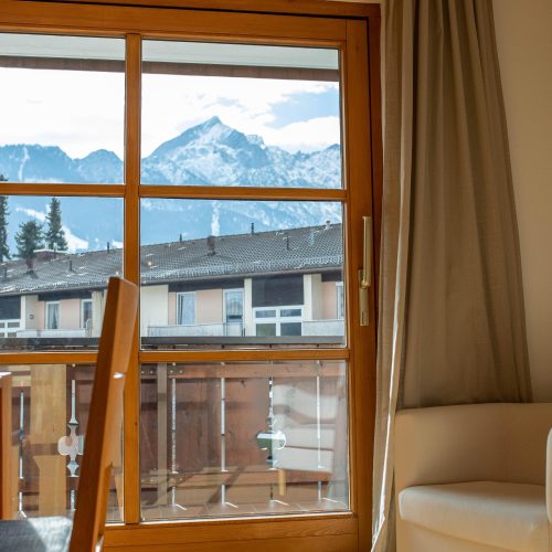 Fenster Ausblick mit einem kleinen weißen Sessel in Ferienwohnung in Garmisch-Partenkirchen