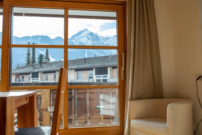 Fenster Ausblick mit einem kleinen weißen Sessel in Ferienwohnung in Garmisch-Partenkirchen