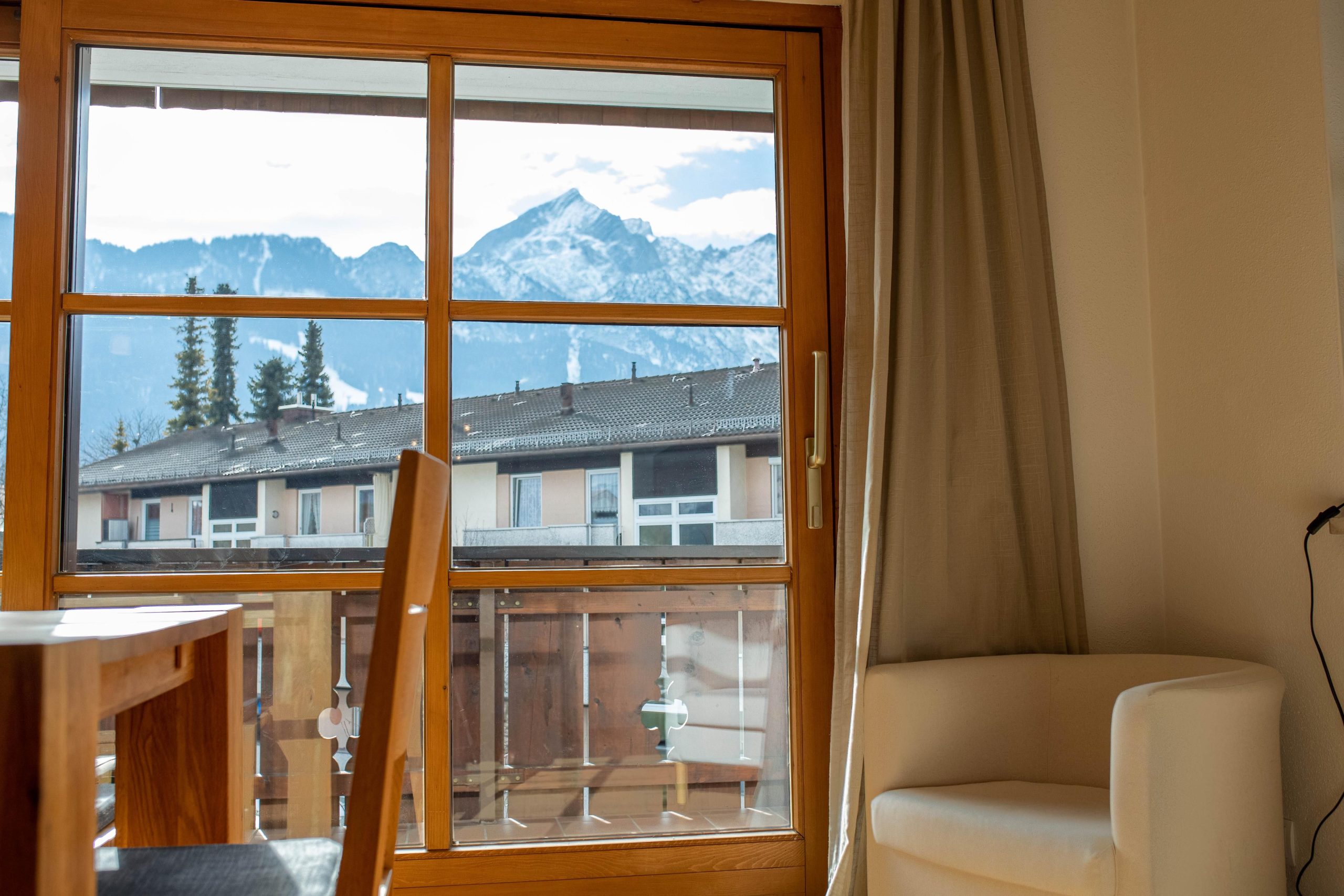 Fenster Ausblick mit einem kleinen weißen Sessel in Ferienwohnung in Garmisch-Partenkirchen