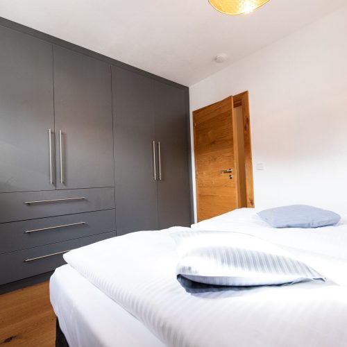 Schlafzimmer mit einem grauen Kleiderschrank und weißen Bett in Ferienwohnung in Garmisch-Partenkirchen