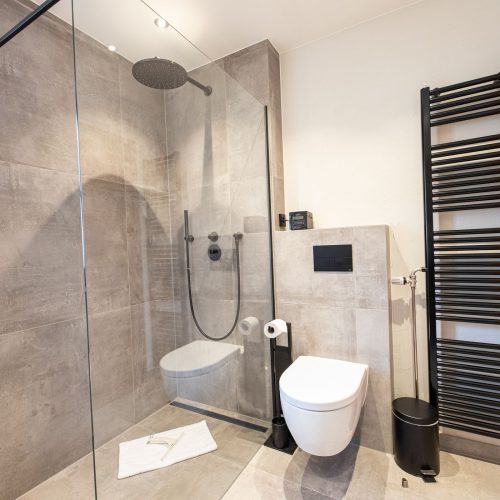 Badezimmer mit grauen Fliesen und einer schwarzen Heizung in Ferienwohnung in Garmisch-Partenkirchen